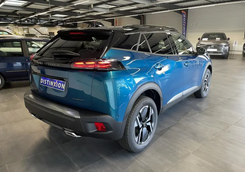 Peugeot 2008 bleu vue 3/4 arrière droit en intérieur avec toit noir et feux arrière LED allumés.