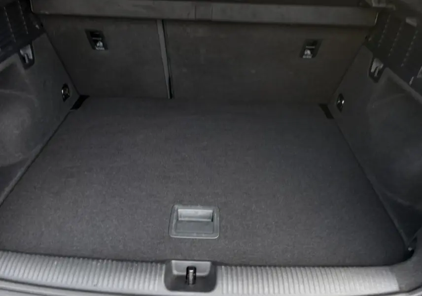Coffre vide de l'Audi Q2 30 TDI S-Line 2025, vue intérieure arrière avec revêtement noir et espace de rangement plat.