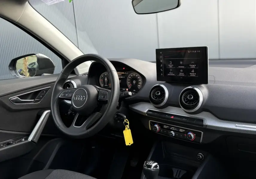 Vue intérieure côté conducteur de l'Audi Q2 30 TDI S-Line 2025 avec volant cuir, écran MMI et levier de vitesse manuel.