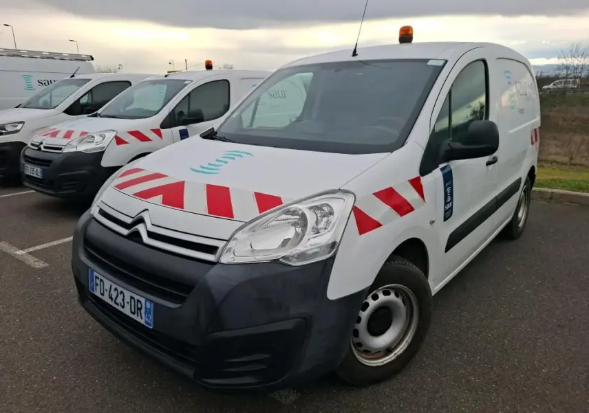 Vue 3/4 avant droit d'un Citroën Berlingo blanc utilitaire avec bandes rouges diagonales et gyrophare orange sur le toit.