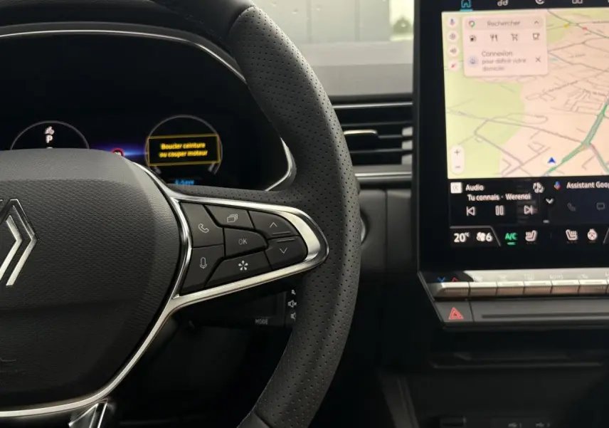 Vue rapprochée du volant perforé et du tableau de bord numérique du Renault Captur blanc nacré, avec écran tactile central affichant la navigation.