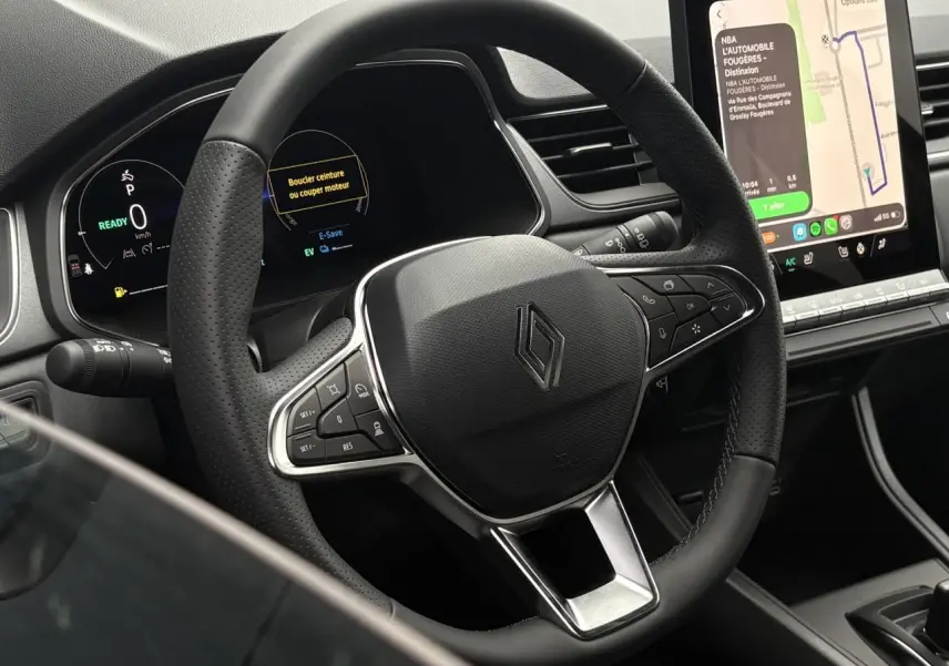 Vue rapprochée du volant noir perforé et du tableau de bord numérique du Renault Captur 2026 avec écran tactile central affichant la navigation.
