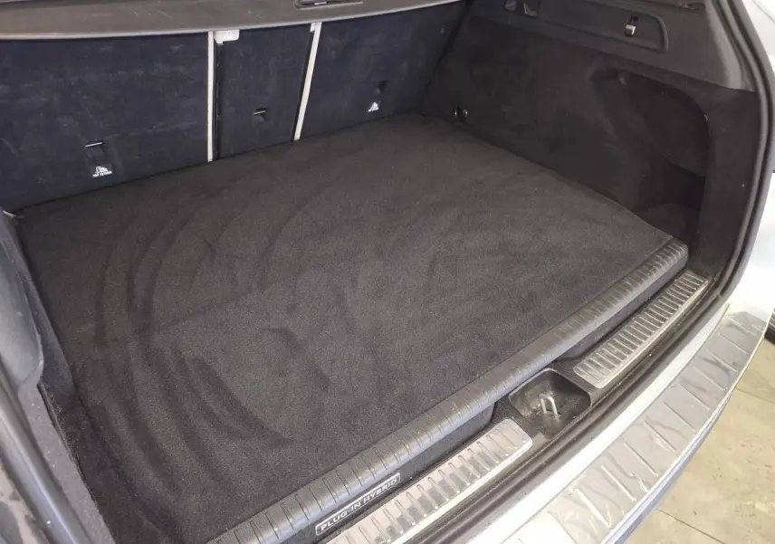 Coffre ouvert vu de dessus d’un Mercedes GLC 350 e gris, avec tapis noir et seuil de chargement inox.