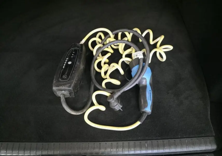 Câble de recharge hybride noir et bleu enroulé dans le coffre noir d'un Mercedes GLC 350 e gris.