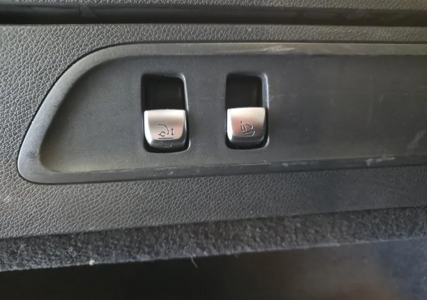 Gros plan sur les commandes argentées d'ouverture du hayon et d'abaissement des sièges dans le coffre d'un Mercedes GLC gris.