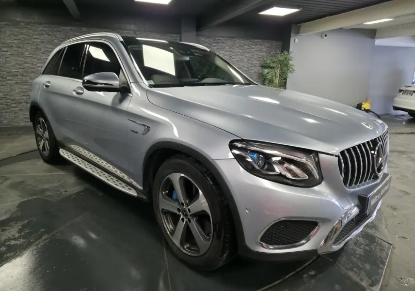Mercedes GLC 350 e gris métallisé en vue 3/4 avant droit, avec jantes alliage 19 pouces et marchepieds inox.