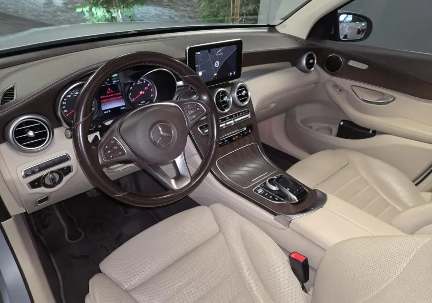 Vue intérieure avant droite du Mercedes GLC 350 e gris, avec tableau de bord en cuir marron et sièges beige perforés.