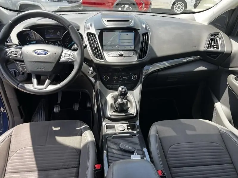 Vue intérieure avant du Ford Kuga bleu foncé 2018, avec tableau de bord, volant multifonction et boîte manuelle visible.