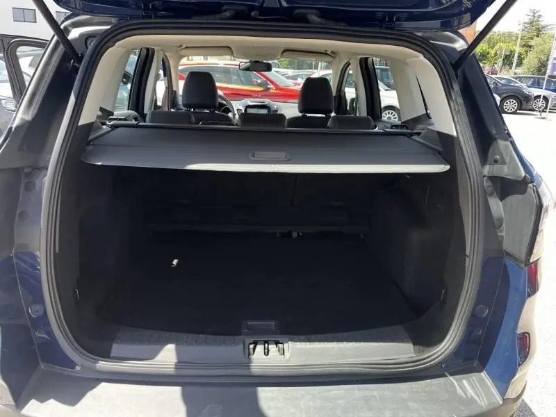 Vue arrière du coffre ouvert d'un Ford Kuga bleu foncé 2018, montrant l'espace de chargement et la tablette cache-bagages.