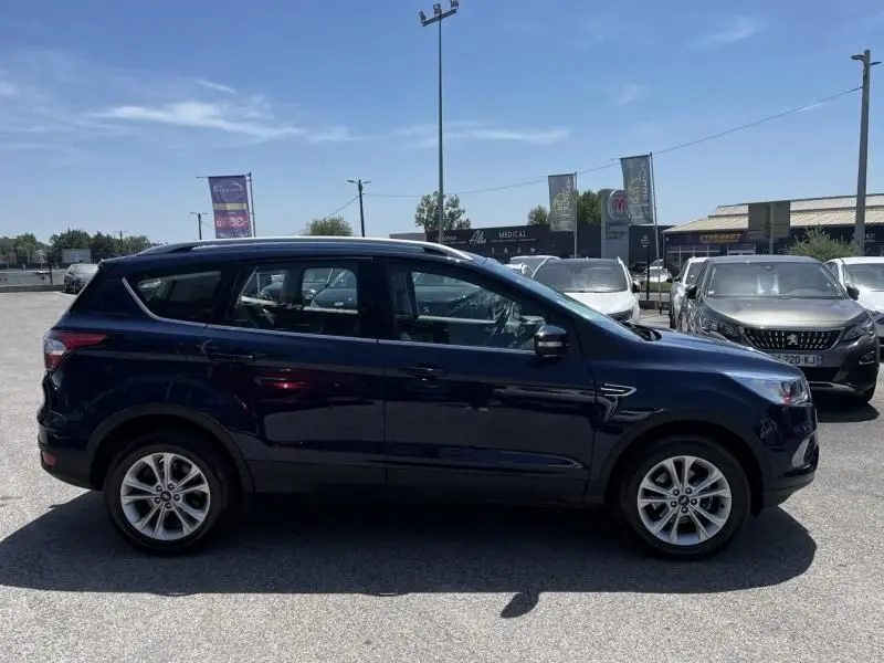 Vue de profil côté gauche d'un Ford Kuga bleu foncé 2018, avec jantes alliage et toit ouvrant visible.