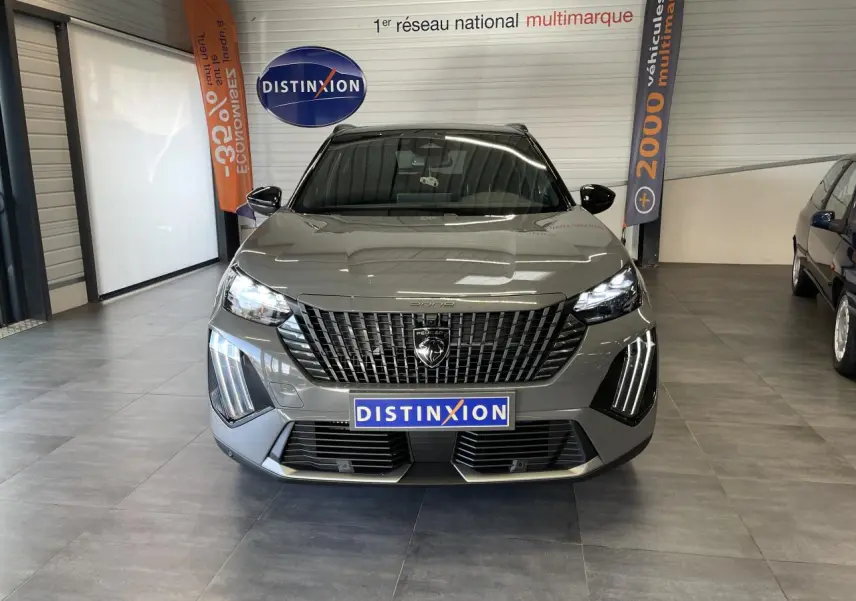 Peugeot 2008 gris en vue frontale, avec calandre noire distinctive et feux LED verticaux allumés en showroom.