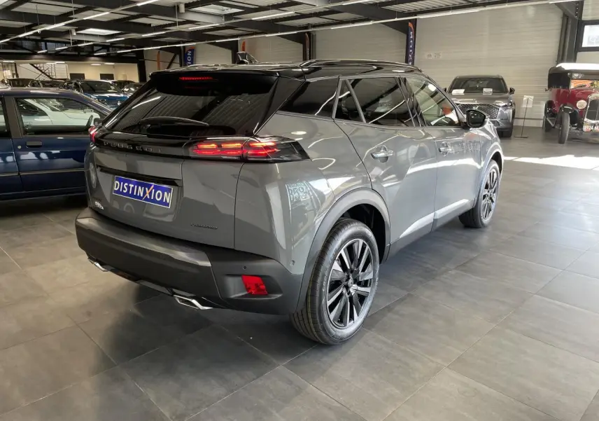 Peugeot 2008 gris en vue 3/4 arrière droit dans un showroom, avec toit noir et feux arrière allumés.
