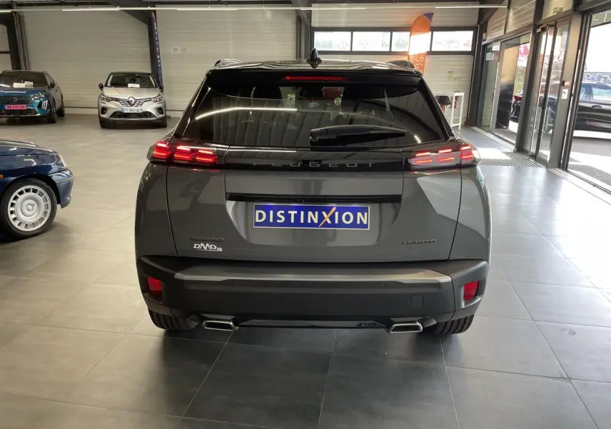 Vue arrière d’un Peugeot 2008 gris hybride 2026 avec feux LED allumés et double sortie d’échappement en concession.