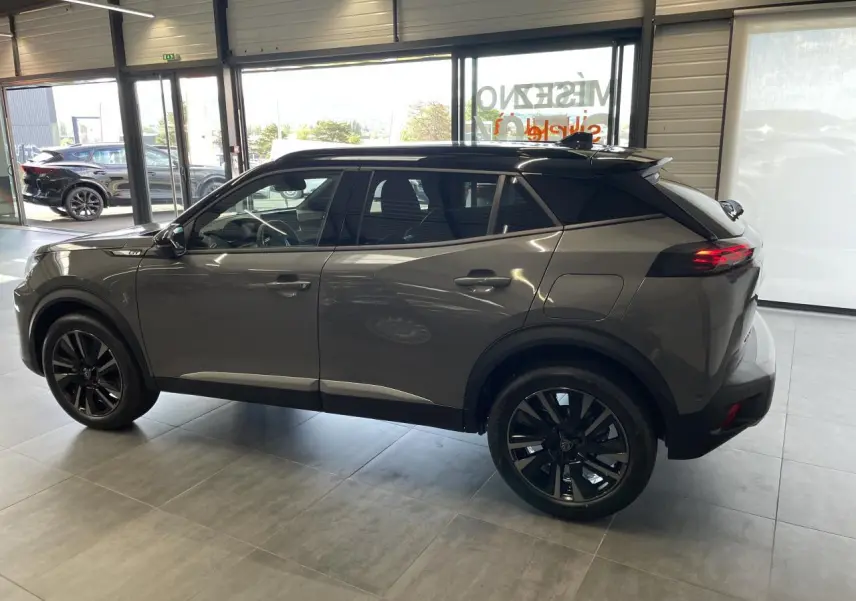 Peugeot 2008 gris en vue de profil côté gauche, avec jantes noires et toit noir contrastant, dans un showroom lumineux.