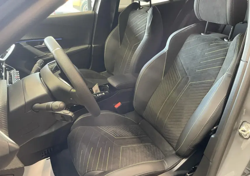 Vue intérieure côté conducteur du Peugeot 2008 gris 2026, sièges sport avec surpiqûres vertes et volant cuir.