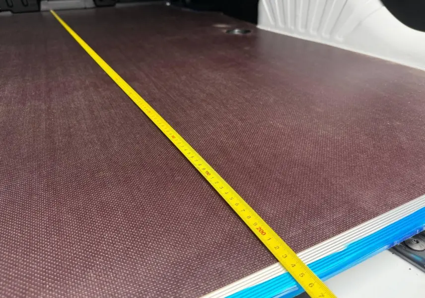 Gros plan sur la surface de chargement brun foncé du Citroën Berlingo Fourgon XL blanc Icy avec un mètre ruban jaune posé dessus.