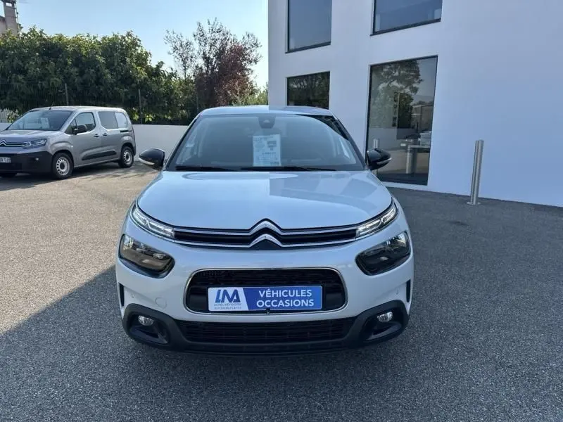 Vue avant d'une Citroën C4 Cactus blanche 2018 avec calandre noire et feux LED distinctifs, stationnée devant un bâtiment.
