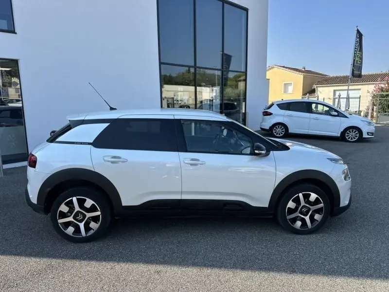 Profil côté gauche d'une Citroën C4 Cactus blanche 2018 avec protections noires et jantes distinctives.