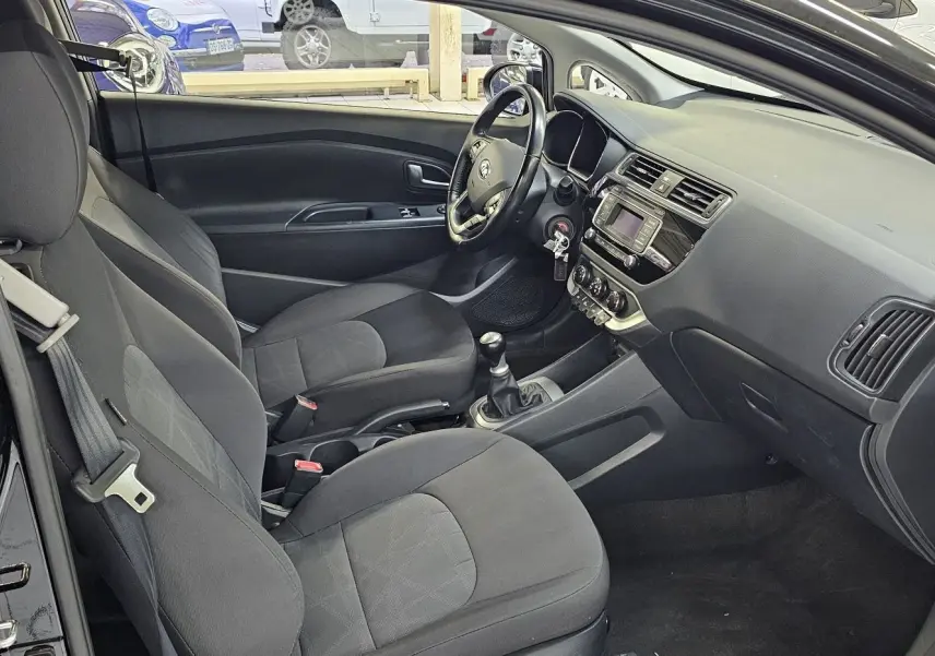 Intérieur noir de la KIA RIO III 3 portes, vue côté conducteur avec tableau de bord et boîte manuelle visibles.