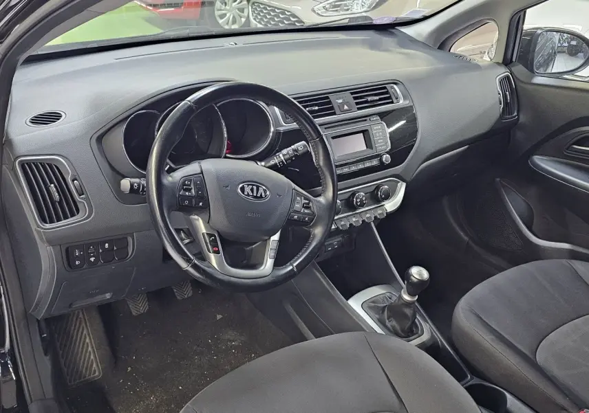 Intérieur de la KIA RIO III 2015 en noir, vue côté conducteur avec volant multifonction et boîte manuelle.