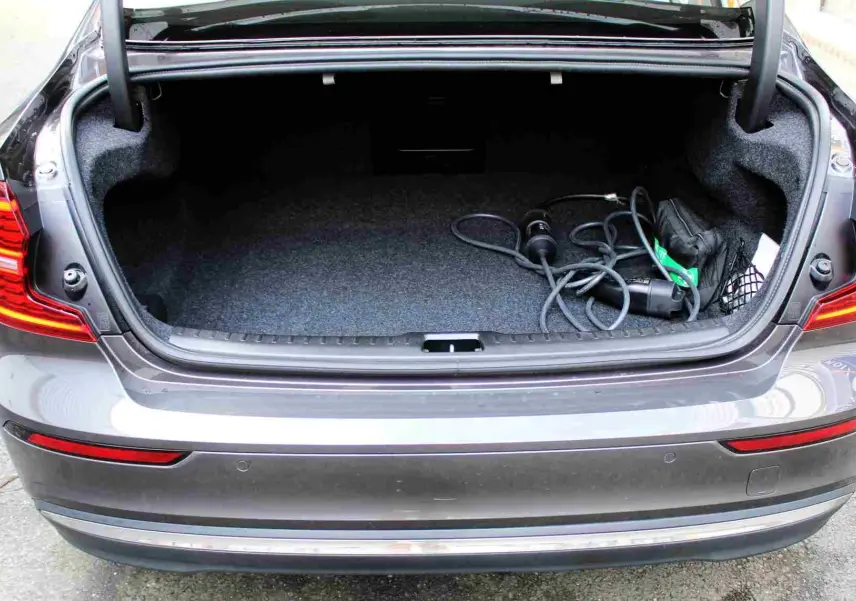 Coffre ouvert vu de l'arrière d'une Volvo S60 T6 hybride rechargeable gris métal avec câble de recharge visible.