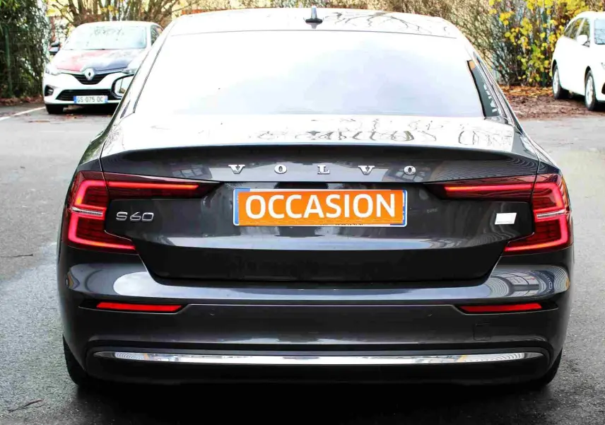 Vue arrière d'une Volvo S60 gris métal 2024 avec feux LED en forme de C et plaque "OCCASION" orange.