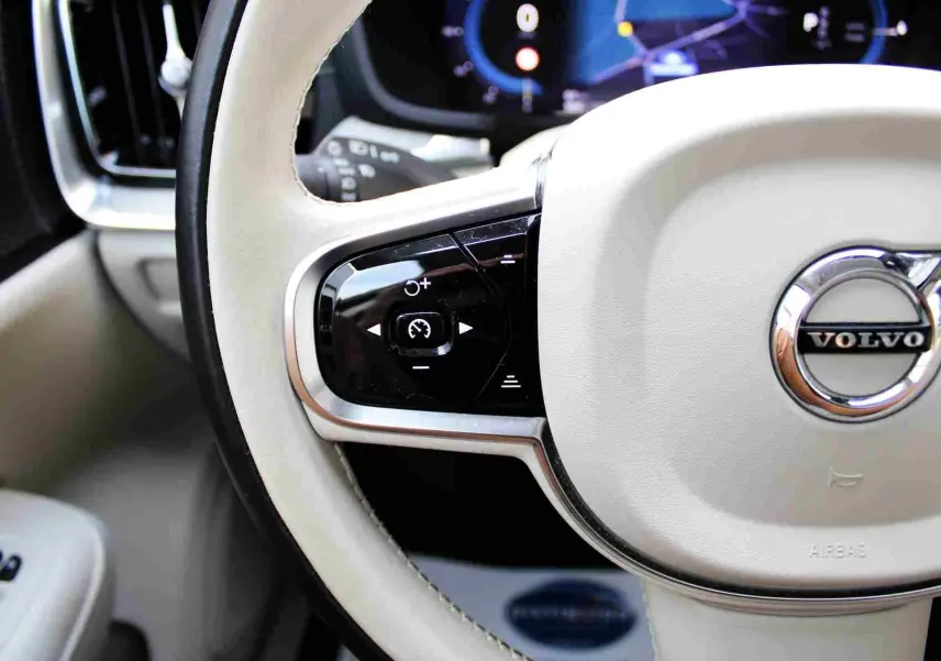 Gros plan sur le volant beige clair du Volvo S60 2024 avec commandes intégrées et logo chromé central.