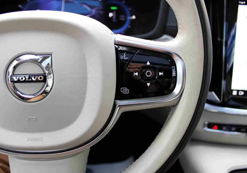 Volant beige clair de Volvo S60 2024 hybride rechargeable, avec commandes intégrées et tableau de bord numérique visible.