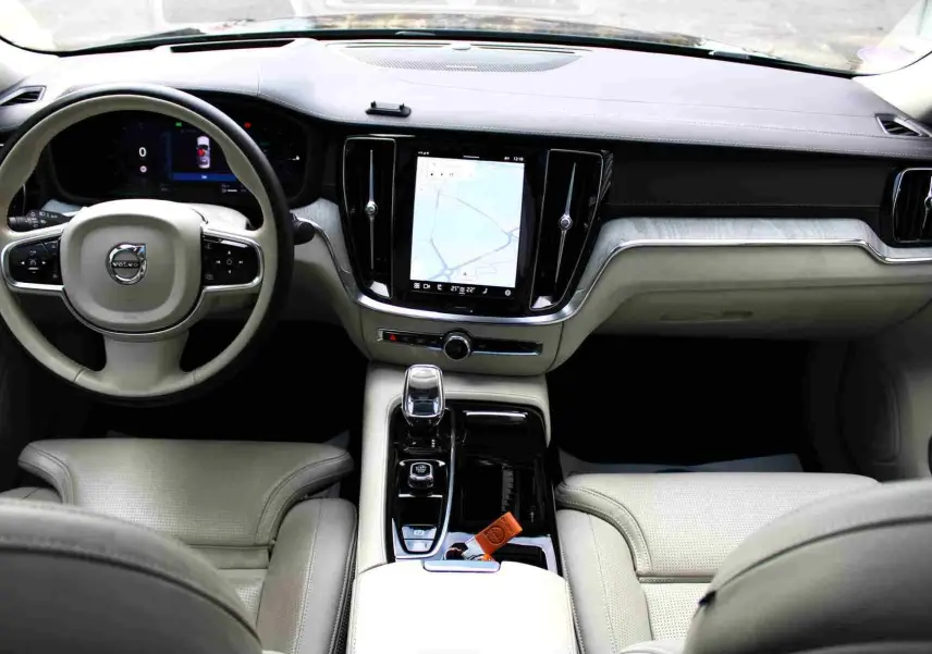 Intérieur clair de la Volvo S60 2024, vue du poste de conduite avec écran central tactile et volant multifonction.
