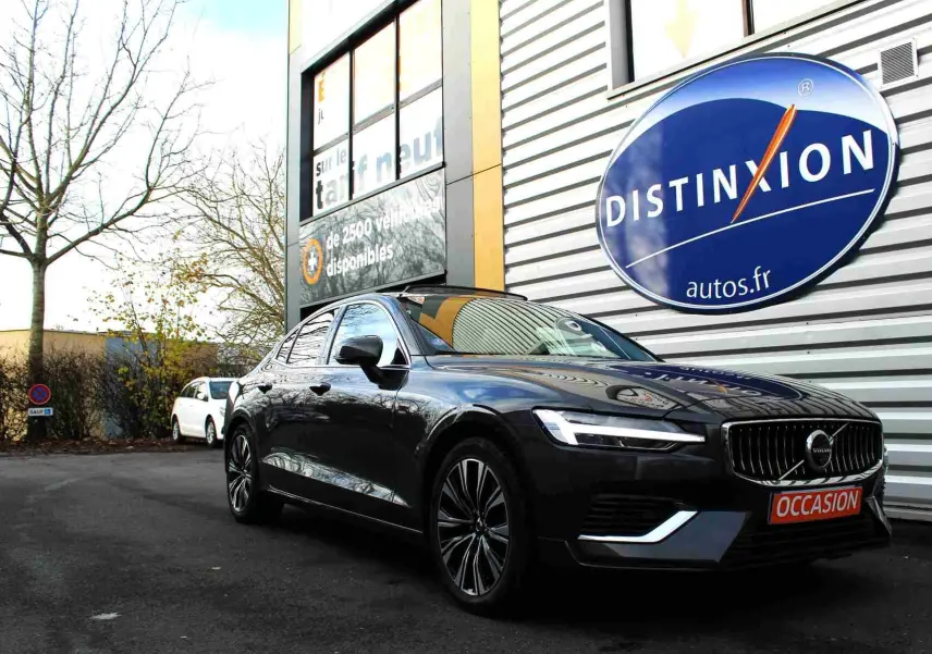 Volvo S60 gris métal vue 3/4 avant droit, avec calandre chromée et plaque "OCCASION" devant un bâtiment commercial.