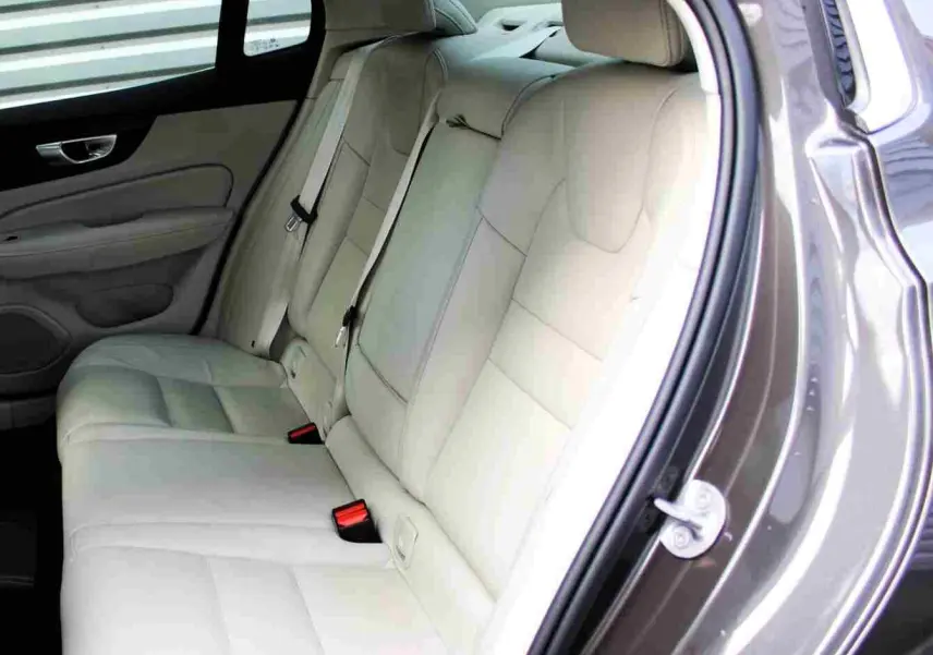 Vue côté droit sur l'intérieur arrière beige clair d'une Volvo S60 2024 gris métal avec sellerie cuir et ceintures visibles.