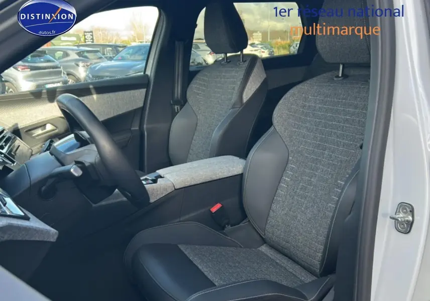 Vue intérieure côté conducteur du Peugeot 5008 blanc okenite, mettant en valeur les sièges tissu et cuir gris avec accoudoir central.