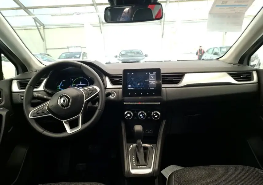 Vue intérieure frontale du tableau de bord du Renault Captur gris Highland 2023 avec écran tactile central et volant multifonction.
