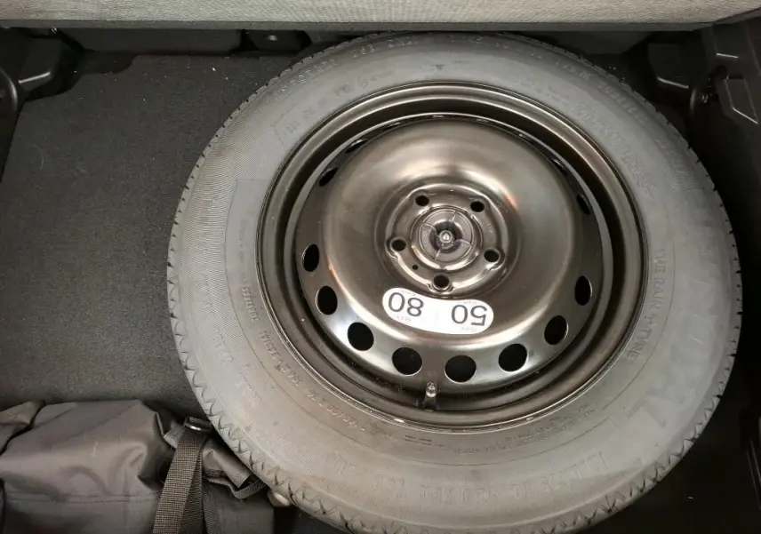 Vue plongeante sur la roue de secours noire en acier du coffre d'un Renault Captur gris Highland 2023.