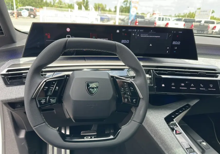 Vue rapprochée du volant cuir multifonctions Peugeot 5008 Hybrid 145 GT avec tableau de bord numérique et console moderne.