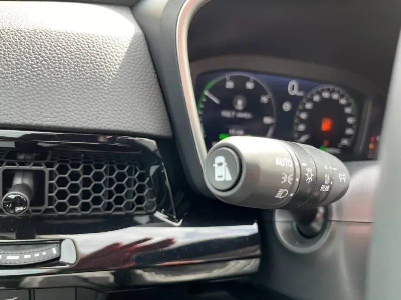 Gros plan sur la commande des feux et l’aération noire en nid d’abeille du tableau de bord du Honda CR-V blanc nacré 2024.