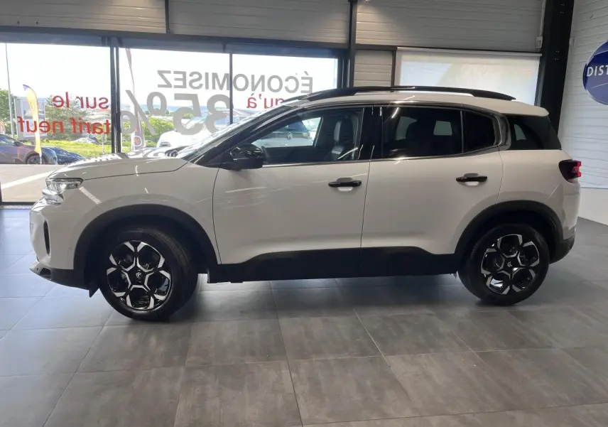 Vue latérale droite d'un Citroën C5 Aircross blanc nacré avec jantes alliage bi-ton et barres de toit noires.