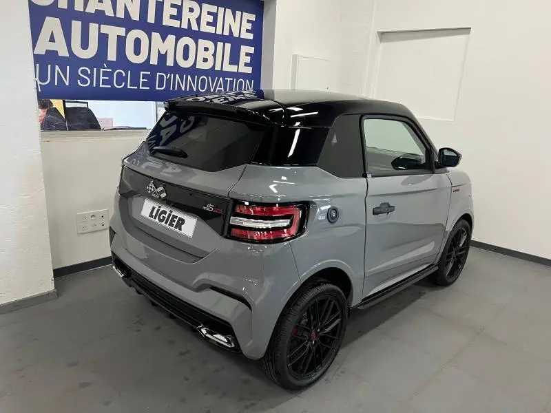 Vue 3/4 arrière droite d'une Ligier JS50 Sport Ultimate E5+ gris avec toit noir et jantes noires en intérieur showroom.