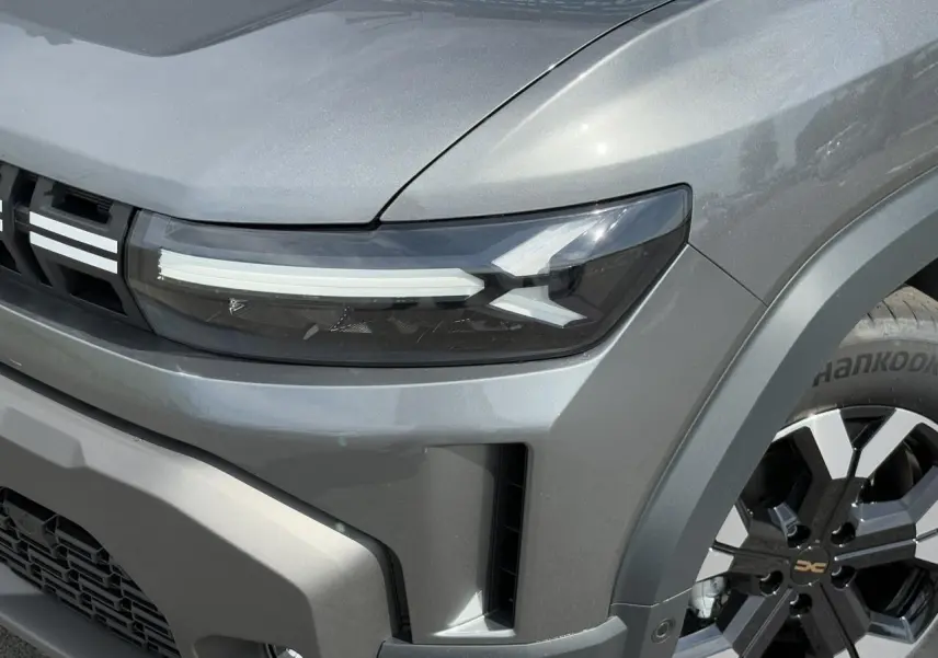 Gros plan sur l'avant droit du Dacia Duster gris schiste, mettant en valeur le phare LED et la jante alliage noire et argentée.