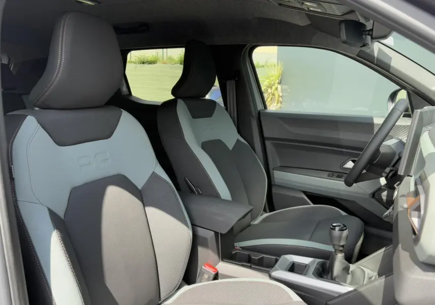 Intérieur du Dacia Duster 2025, vue côté droit sur sièges TEP bicolores gris et noir avec console centrale et levier manuel.