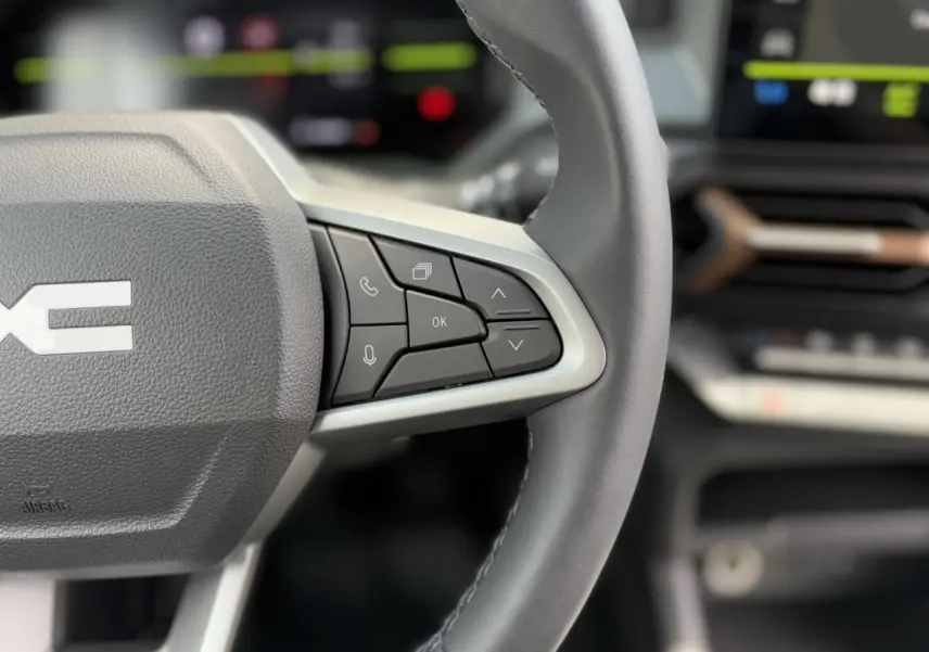 Gros plan sur le volant gris du Dacia Duster 2025, mettant en valeur les commandes multifonctions côté droit.