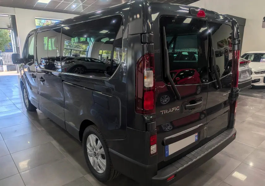 Vue 3/4 arrière droite du Renault Trafic Combi gris comète 2025 en showroom avec vitres teintées et hayon vitré.