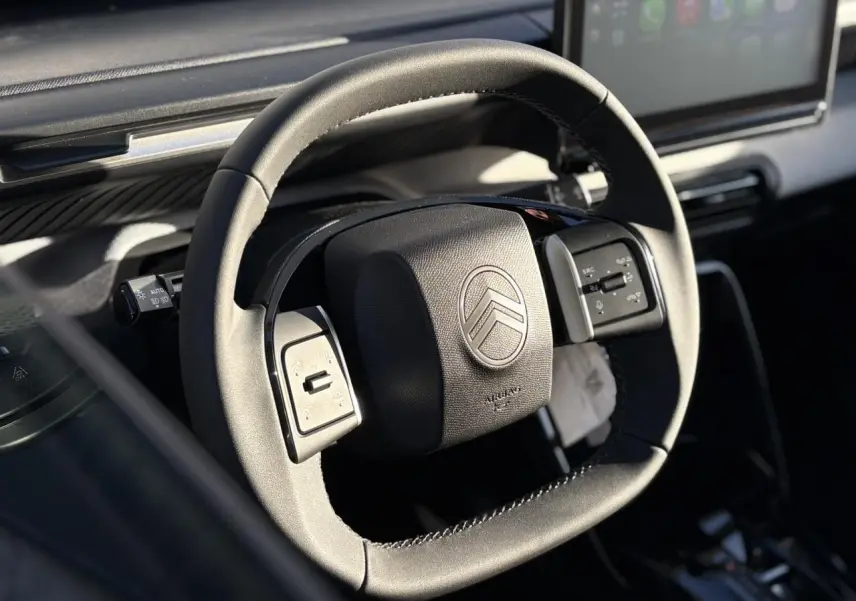 Gros plan sur le volant multifonctions noir du Citroën C3 Aircross Hybrid 2025 avec écran tactile en arrière-plan.