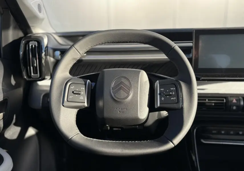 Vue rapprochée du volant noir de la Citroën C3 Aircross 2025 avec commandes multifonctions et tableau de bord gris.