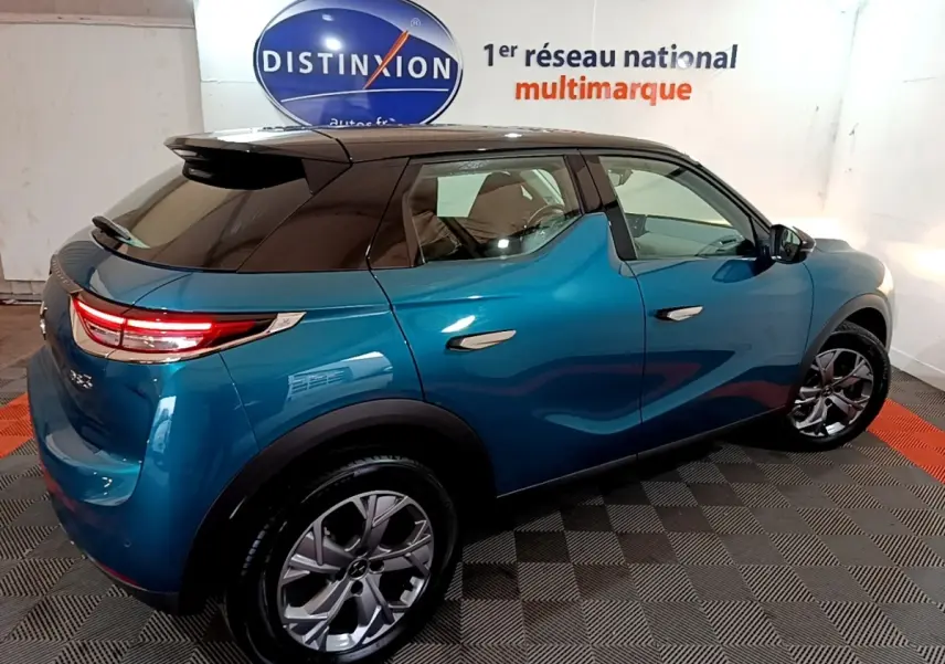 Vue 3/4 arrière droite d'un DS3 Crossback bleu avec toit noir et feux arrière LED dans un showroom.