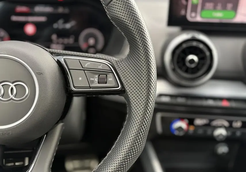 Gros plan sur le volant en cuir perforé de l’Audi Q2 rouge 2025, avec commandes multifonctions visibles.