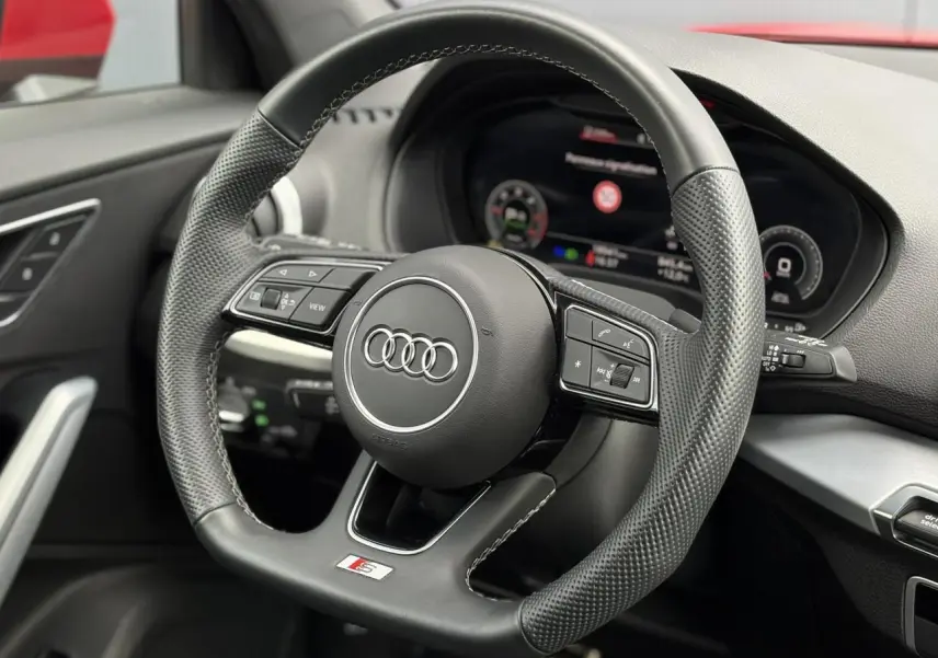 Vue rapprochée du volant cuir perforé S-Line de l'Audi Q2 35 TDI 150, avec tableau de bord numérique en arrière-plan.