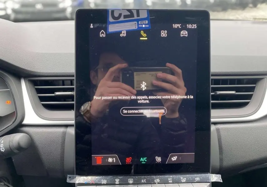 Vue rapprochée de l'écran tactile central du tableau de bord du Renault Captur 2025 avec commandes climatisation et ventilation visibles.