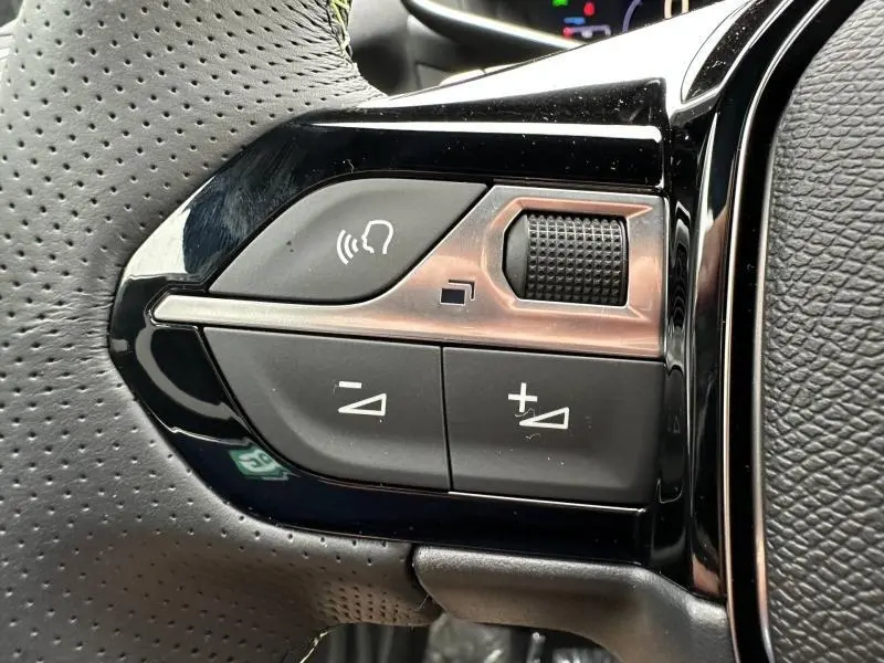 Gros plan sur les commandes de volume et de reconnaissance vocale sur le volant perforé gris du Peugeot 2008 Hybrid 2025.