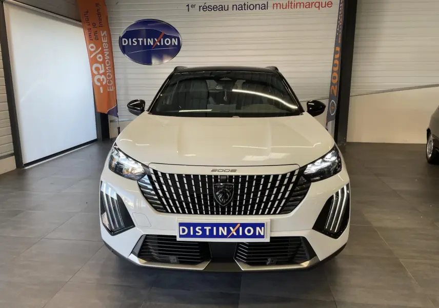 Vue frontale d'un Peugeot 2008 blanc avec calandre noire à motifs verticaux et feux LED en griffes, en intérieur showroom.